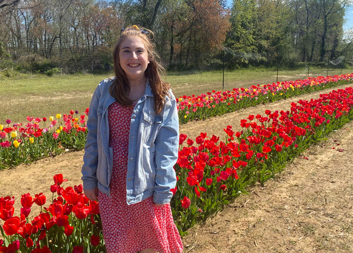 young woman standing in front of red flowers