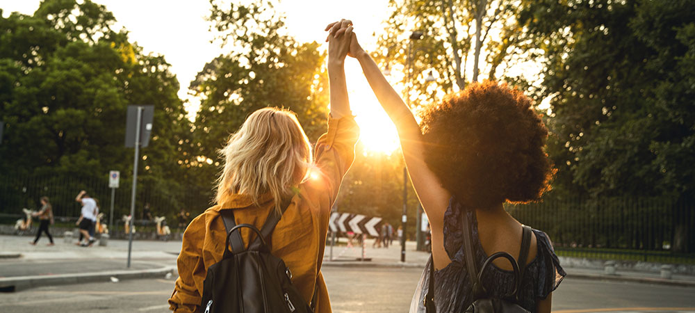 two women facing away from camera with hands clasped and raised to the sky