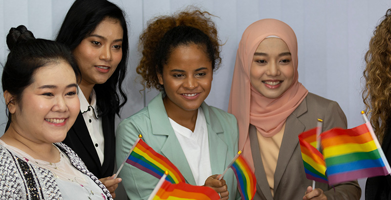 four women smiling and waving rainbow flags