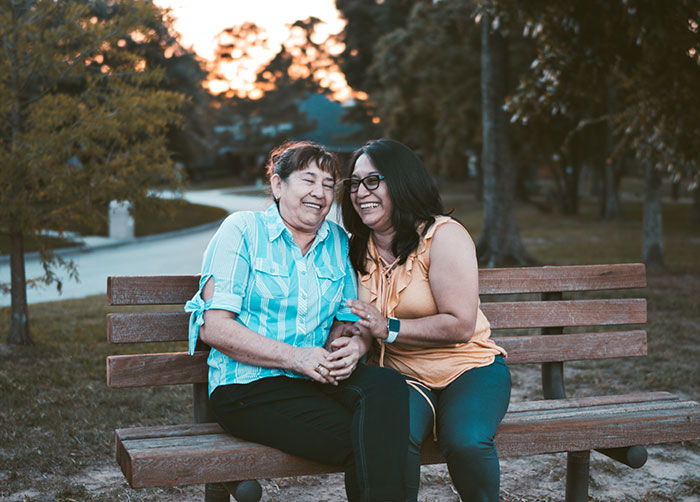 two older women laughing together on a park bench