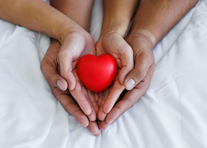 two people with hands cupped together holding a small red heart