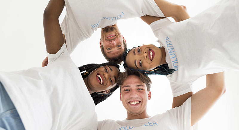 four young adults standing in circle smiling looking down at camera