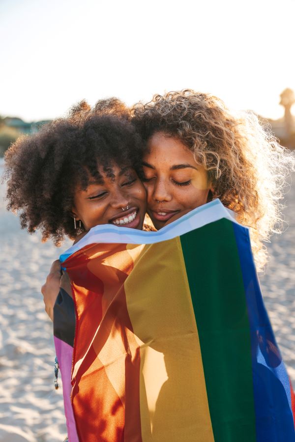 two women embracing with a pride flag wrapped around them