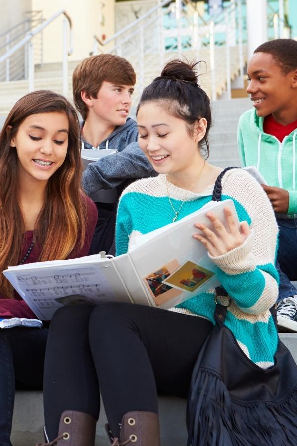 four students talking while sitting on stairs outside of school