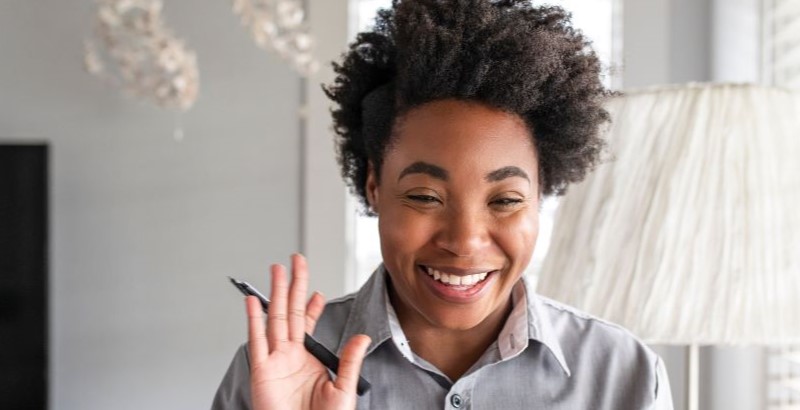 a woman waves at her screen during a video therapy session